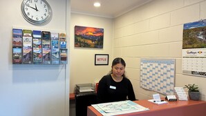 A reception desk with a clock, a calendar, and various informational posters on the wall. - Charlies Motor Lodge (Balclutha)
