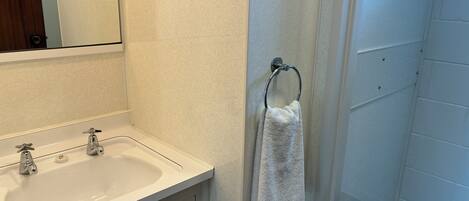 A bathroom with a sink, mirror, towel rack, and shower area.