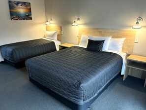 Une chambre d’hôtel avec deux lits, des têtes de lit en bois, des lampes de chevet, un tableau au mur et un sol recouvert de moquette.
