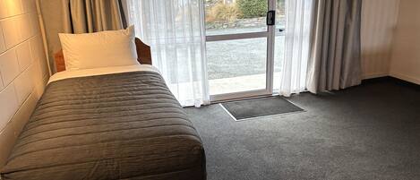 Una habitación con una cama, una ventana con cortinas, un televisor y una puerta.