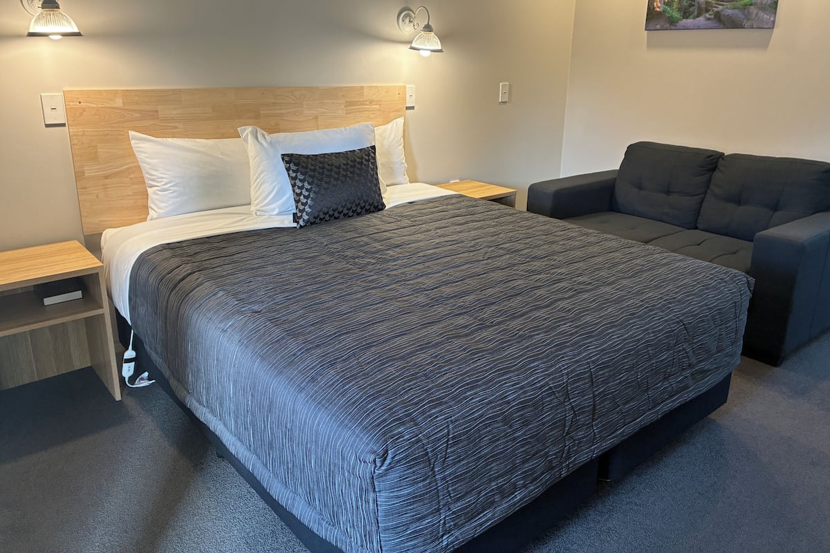 Una habitación de hotel con cama, mesitas de noche, un sofá y un cuadro colgado en la pared.