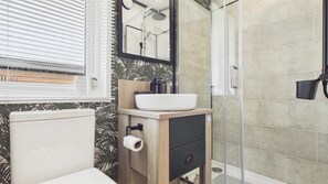 Un baño con inodoro, lavamanos con espejo y zona de ducha.