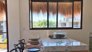 A dining area with a wooden table, black chairs, and a large window with a view of greenery and buildings. - MHV Milagres - Guadalupe 08 (Passo de Camaragibe)