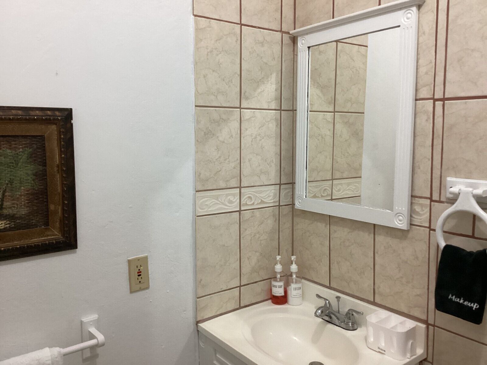 A bathroom with a white sink, a mirror, and a towel rack with a black towel labeled "Makeup".