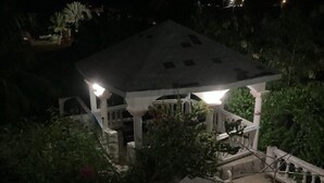 A gazebo with a tiled roof and white columns, surrounded by greenery.
