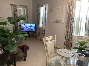 A living room with a television, a glass table, chairs, and a large plant. - Colwin's Place (Cockburn Town)