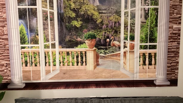 A room with a large window overlooking a scenic outdoor view, a dark green sofa, and a decorative wall.