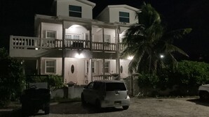 A two-story building with a balcony, a car parked in front, and a palm tree nearby.