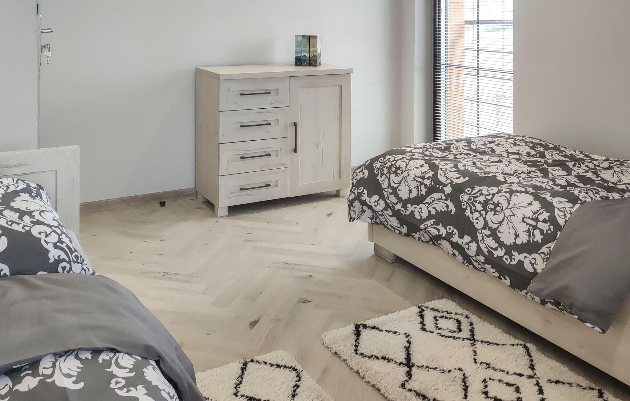 A bedroom with a bed, a dresser, and a window with blinds.