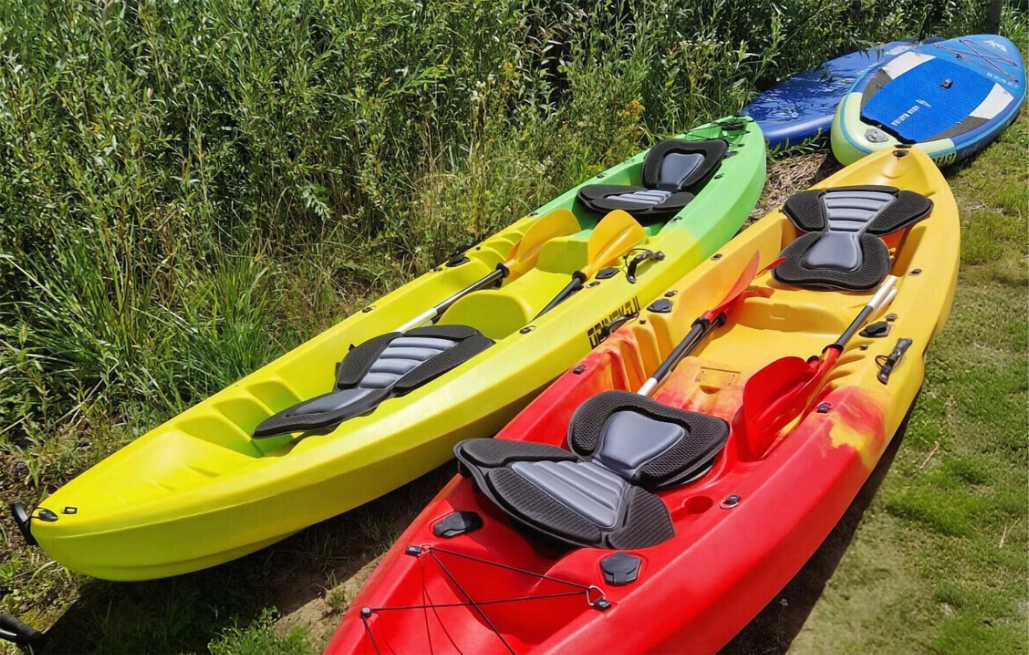 Three kayaks lined up on grass.