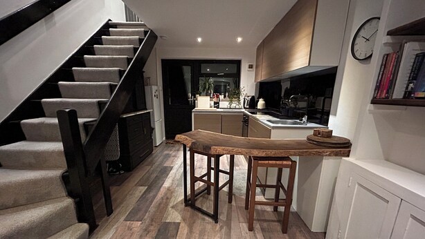 Une cuisine moderne avec un banc en bois, un escalier et une horloge au mur.