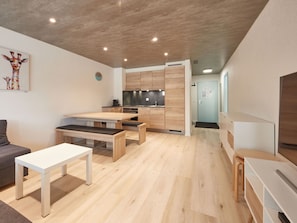 Eine moderne Küche mit Holzschränken und einem eingebauten Ofen. Es gibt einen Essbereich mit einem weißen Tisch und Bänken.