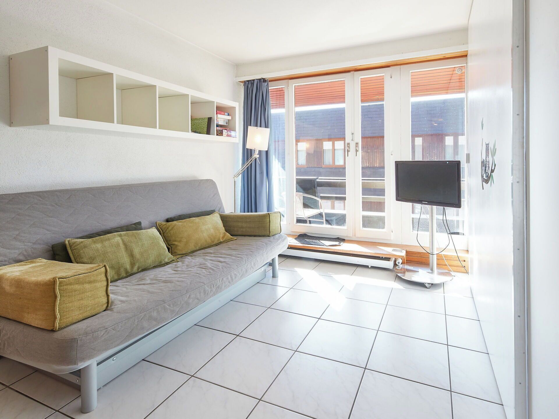 Una sala de estar moderna con un sofá gris, un televisor de pantalla plana y un ventanal corredero que da a un espacio al aire libre.