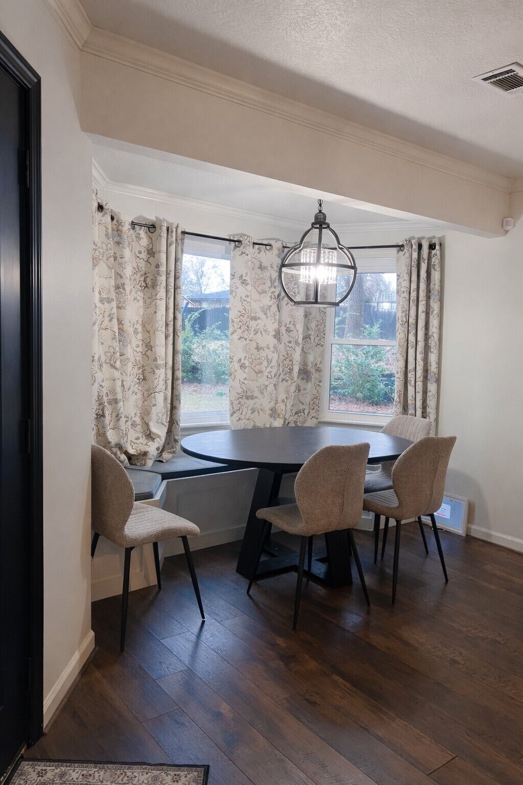 A dining area with a round table, four chairs, and a hanging light fixture.