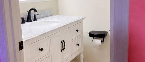 A bathroom with a white vanity, a mirror, a black towel rack, and a colorful rug.