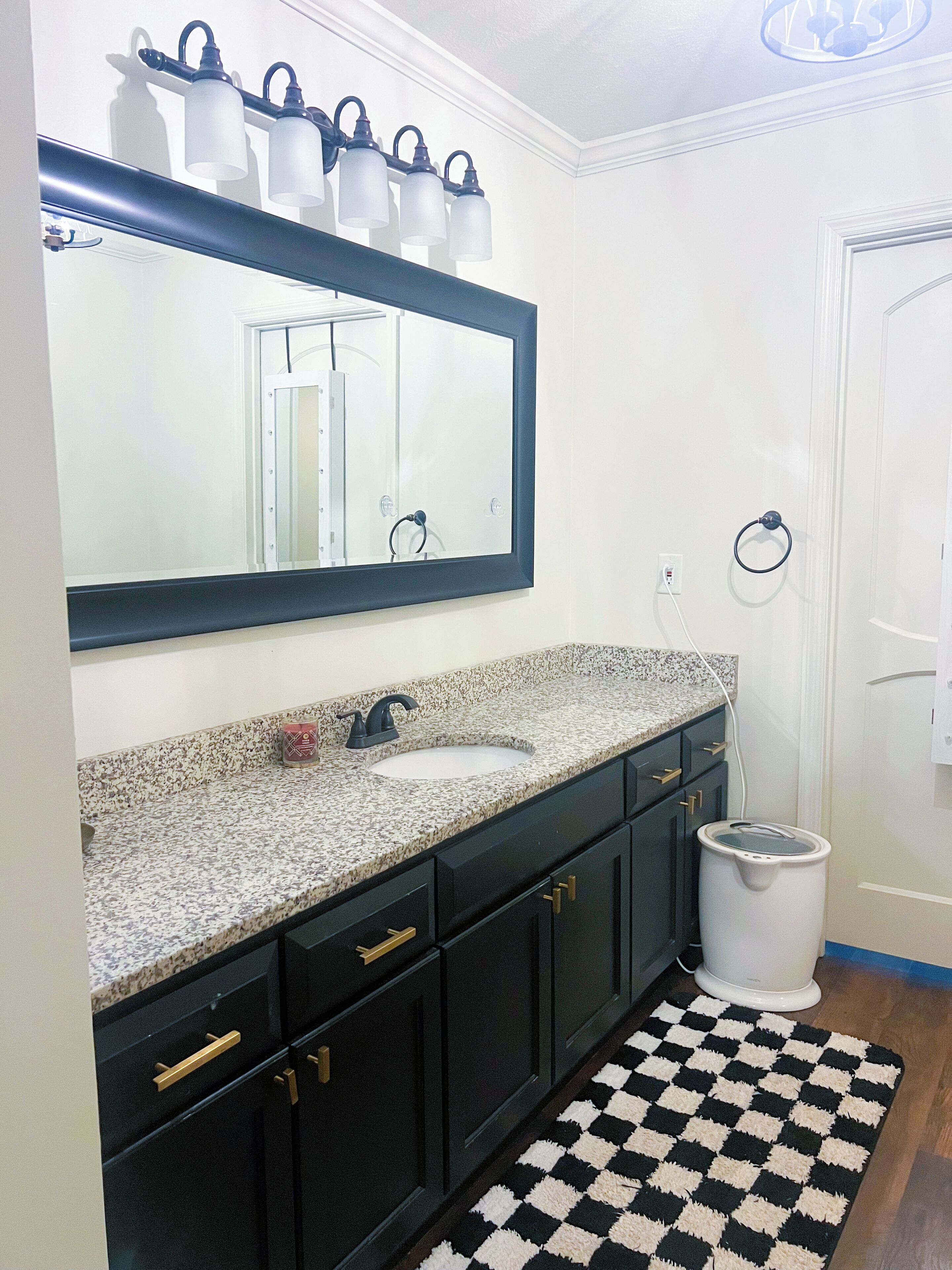 Un baño con un lavamanos blanco, muebles oscuros, un espejo y un tapete a cuadros blanco y negro.