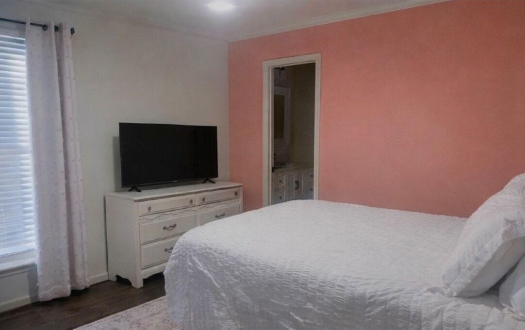 A bedroom with a bed, a television on a dresser, a mirror, and a door.