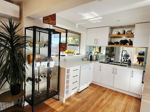 A modern kitchen with white cabinets, a dishwasher, and a sink. There is a plant on the left and a wooden floor. - Luxury Panorama Spa & Sauna Retreat with Blue Mountains Views (Wentworth Falls)