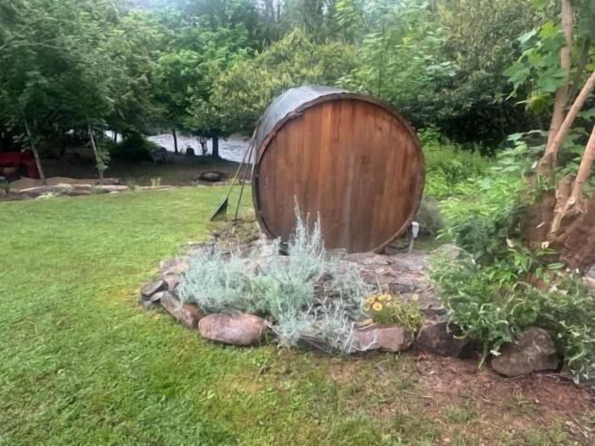 A rustic wooden barrel in a garden setting with surrounding greenery and rocks.