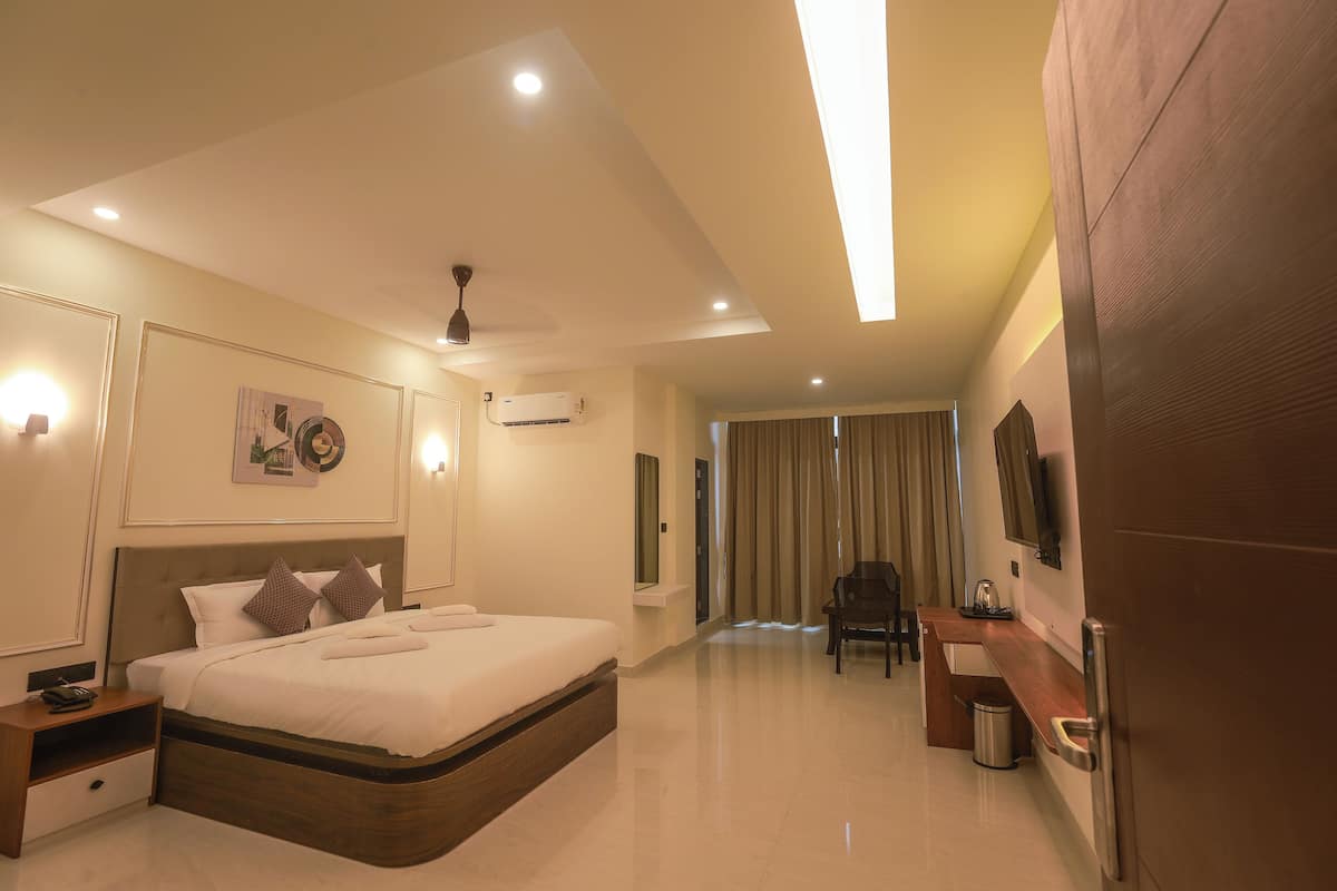 A modern hotel room with a large bed, bedside tables, a desk, a chair, a TV, and a ceiling fan.