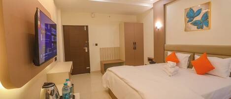 A hotel room with a bed, a TV mounted on the wall, a ceiling fan, and a painting on the wall.