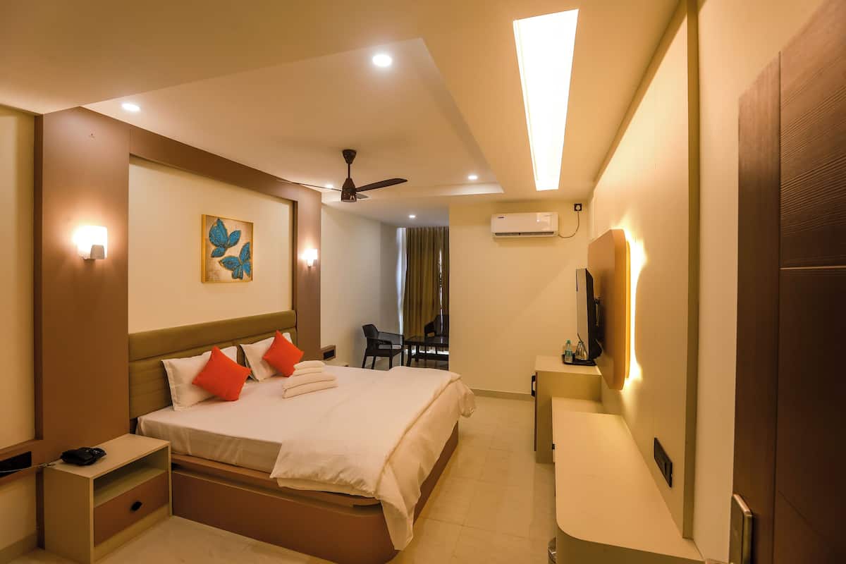 A hotel room with a bed, bedside table, wall-mounted TV, ceiling fan, and a painting.