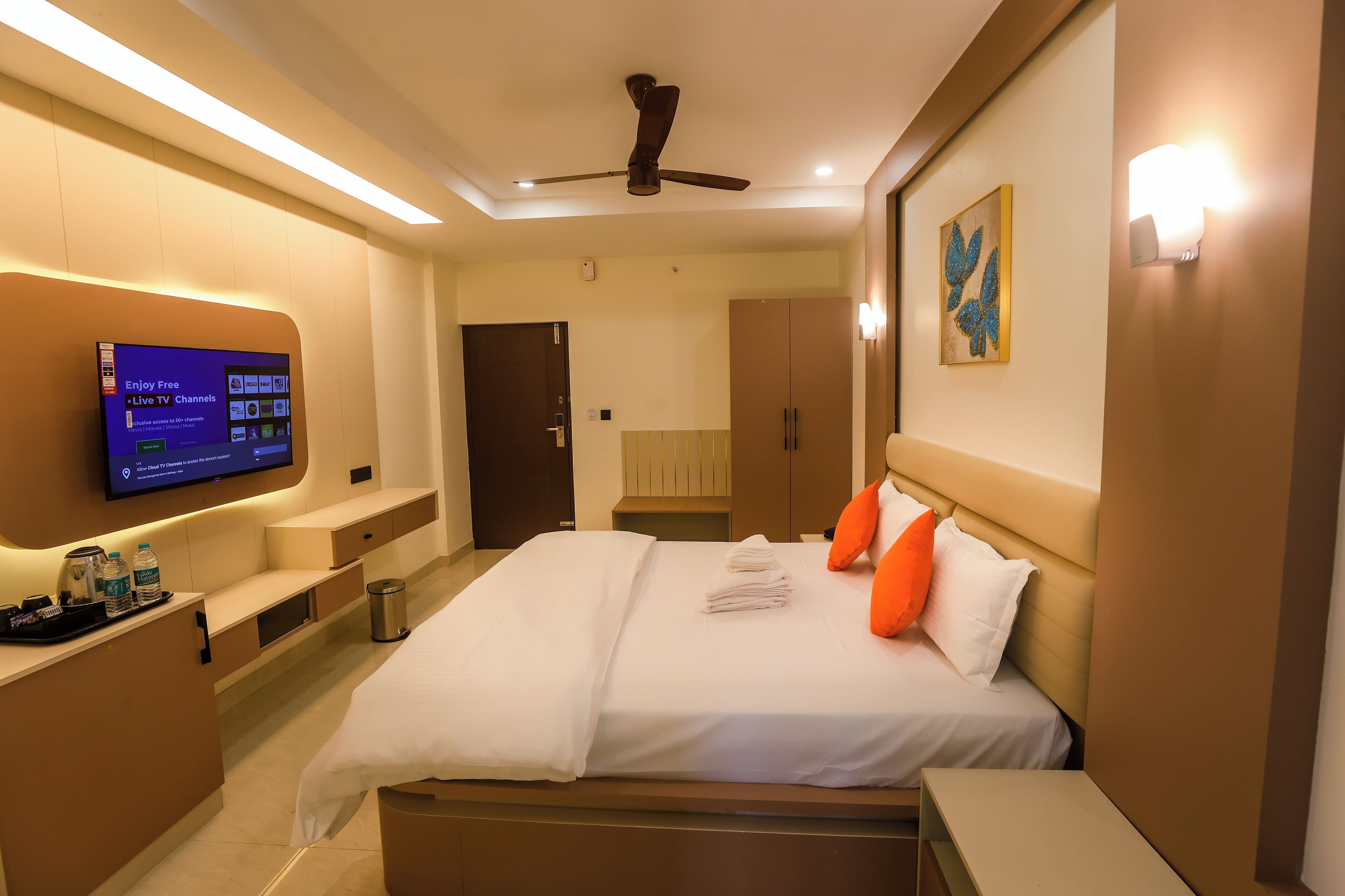 A hotel room with a bed, a TV mounted on the wall, a ceiling fan, and a small table with a tray.