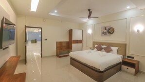 Une chambre d’hôtel moderne dotée d’un grand lit, de tables de chevet, d’un ventilateur de plafond et d’un téléviseur à écran plat fixé au mur.
