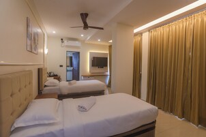 Habitación de hotel con dos camas, ventilador de techo, televisión de pantalla plana y una ventana grande con cortinas.