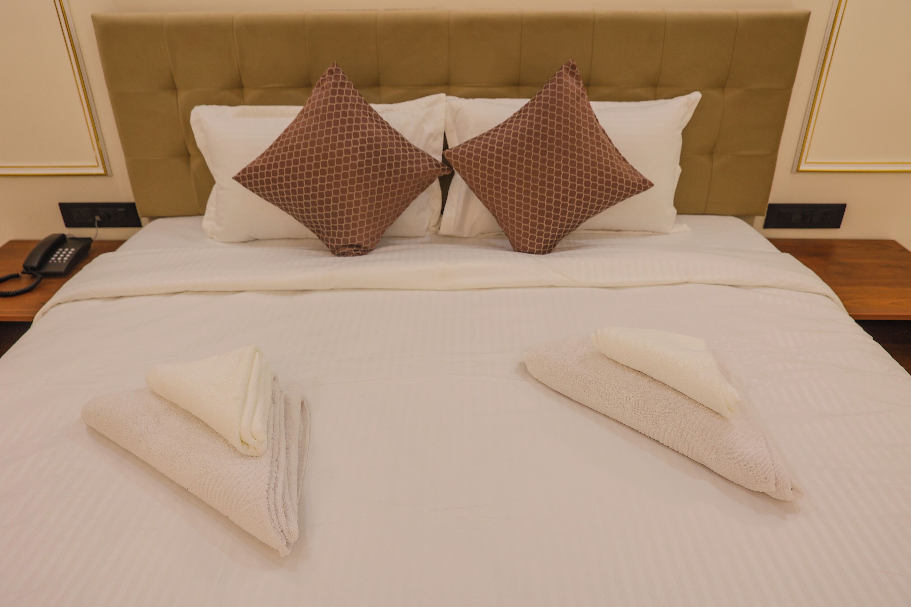 A neatly made bed with a headboard, two pillows, and two folded towels.