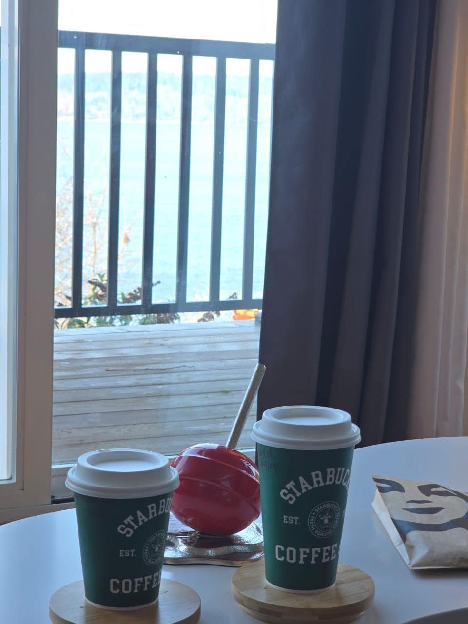 Due tazze da caffè Starbucks su un tavolo con vista su un pontile di legno e una ringhiera.