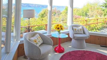 A sunroom with two chairs, a red table, and a view of the outdoors.