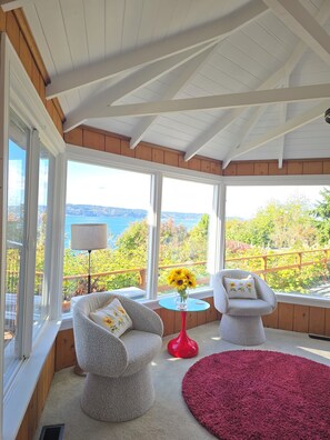 Une véranda avec deux fauteuils, une table rouge et une vue sur l’extérieur.
