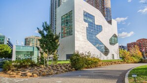 A modern building with a unique angular design, surrounded by other high-rise buildings and a well-maintained park area. - Blueground | Long Island City, pool, nr Gantry Plaza (New York)