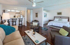 A modern hotel room with a bed, a sofa, a coffee table, a dining area, and a kitchen. - Sans Souci 805—Unbeatable Pacific Ocean front King Villa Sleeps 3—8thFL⁓MONTHLY⁓ (Honolulu)