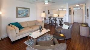 Een woonkamer met een bank, salontafel en fauteuil, een keuken met barstoelen, en een eettafel.