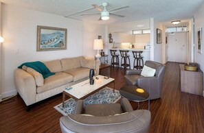 A living room with a sofa, coffee table, and armchair, a kitchen area with bar stools, and a dining table. - Sans Souci 805—Unbeatable Pacific Ocean front King Villa Sleeps 3—8thFL⁓MONTHLY⁓ (Honolulu)