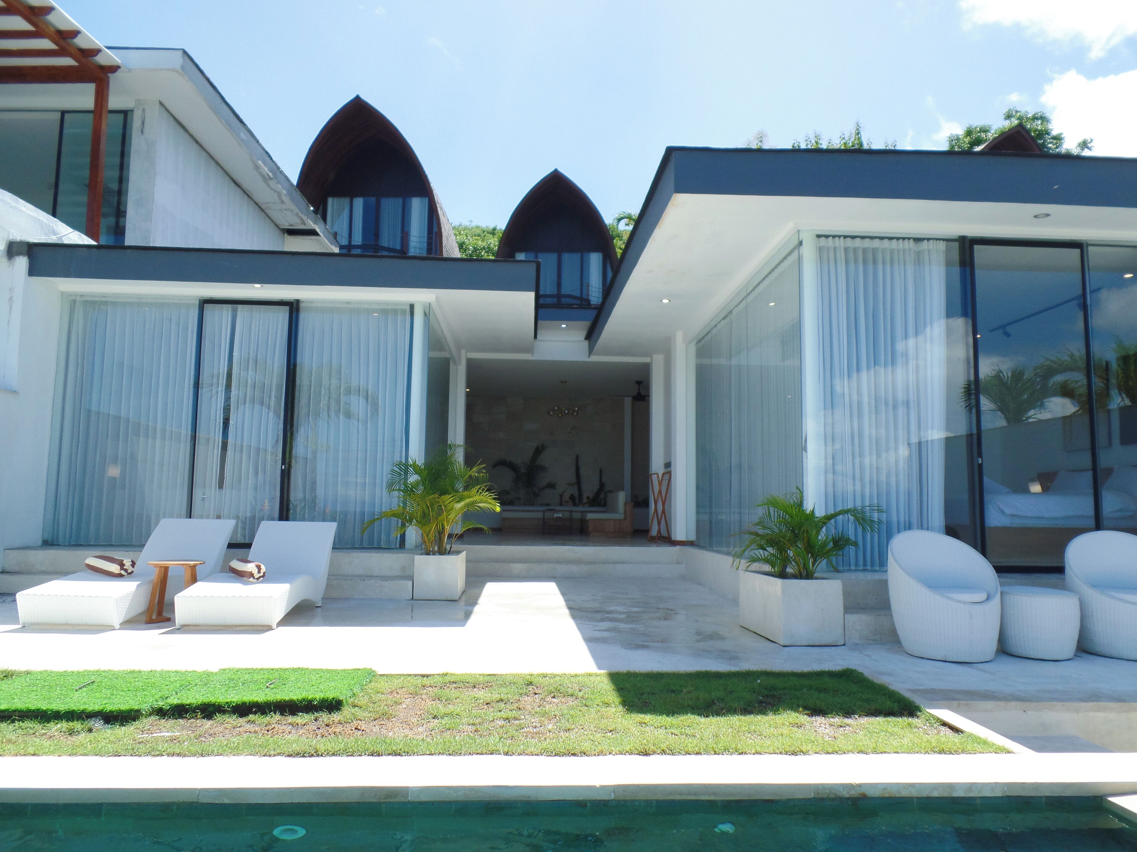 A modern house with a swimming pool, outdoor seating, and a view of the interior.