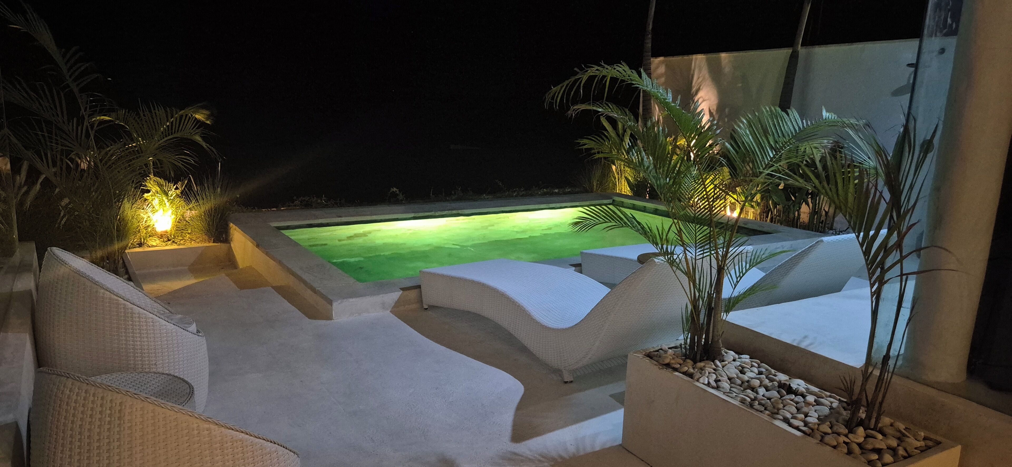 A nighttime outdoor area with a swimming pool, lounge chairs, and potted plants.