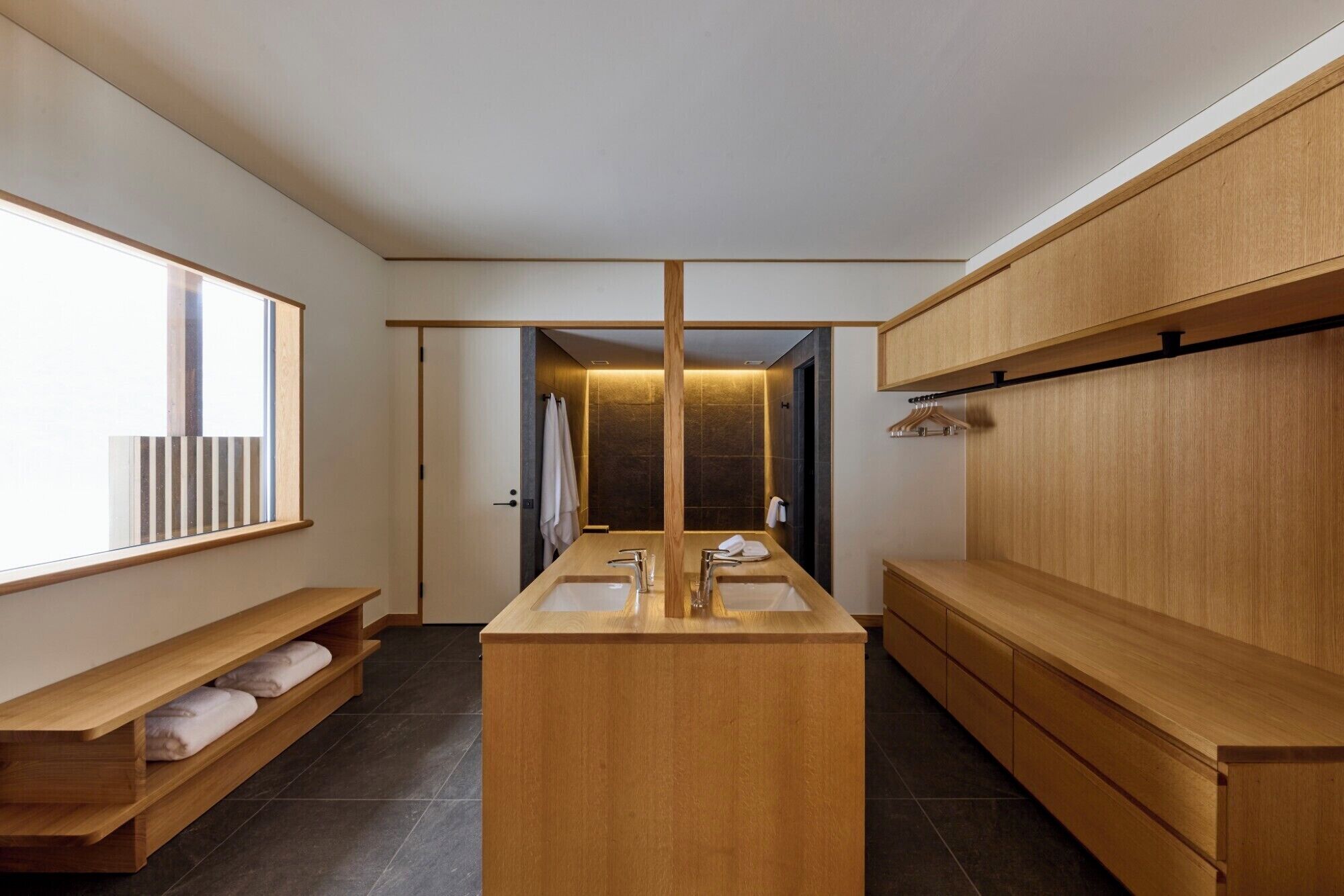 Un baño moderno con un lavamanos central, muebles de madera y un banco con toallas.