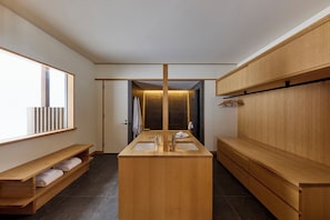 A modern bathroom with a central sink, wooden cabinetry, and a bench with towels.