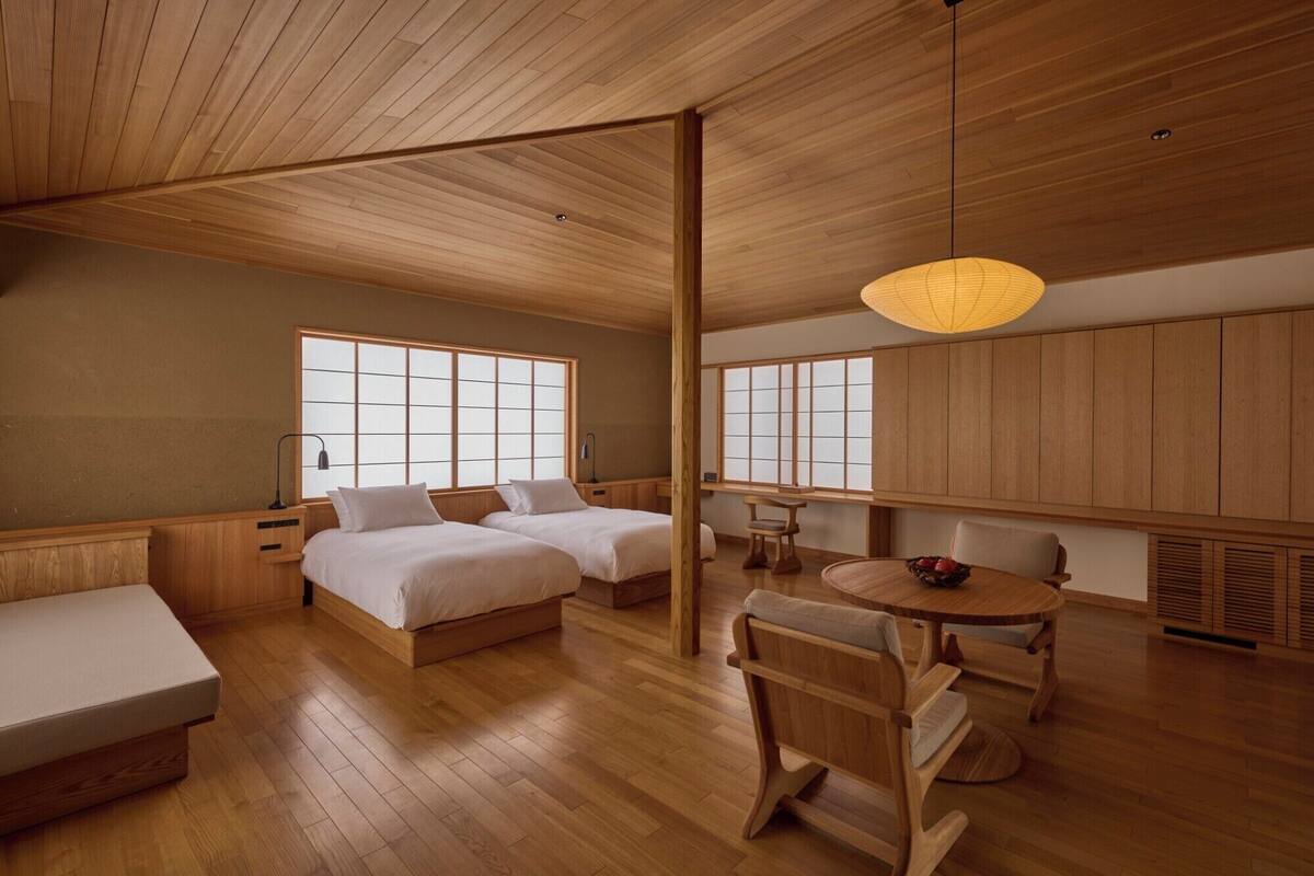 Ein traditionell eingerichteter japanischer Raum mit Holzboden, zwei Betten, einem Esstisch und einem großen Fenster.