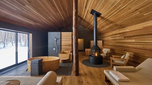Un intérieur moderne avec un plafond lambrissé en bois, une cheminée en pierre, un sauna et une grande fenêtre donnant sur un paysage enneigé.