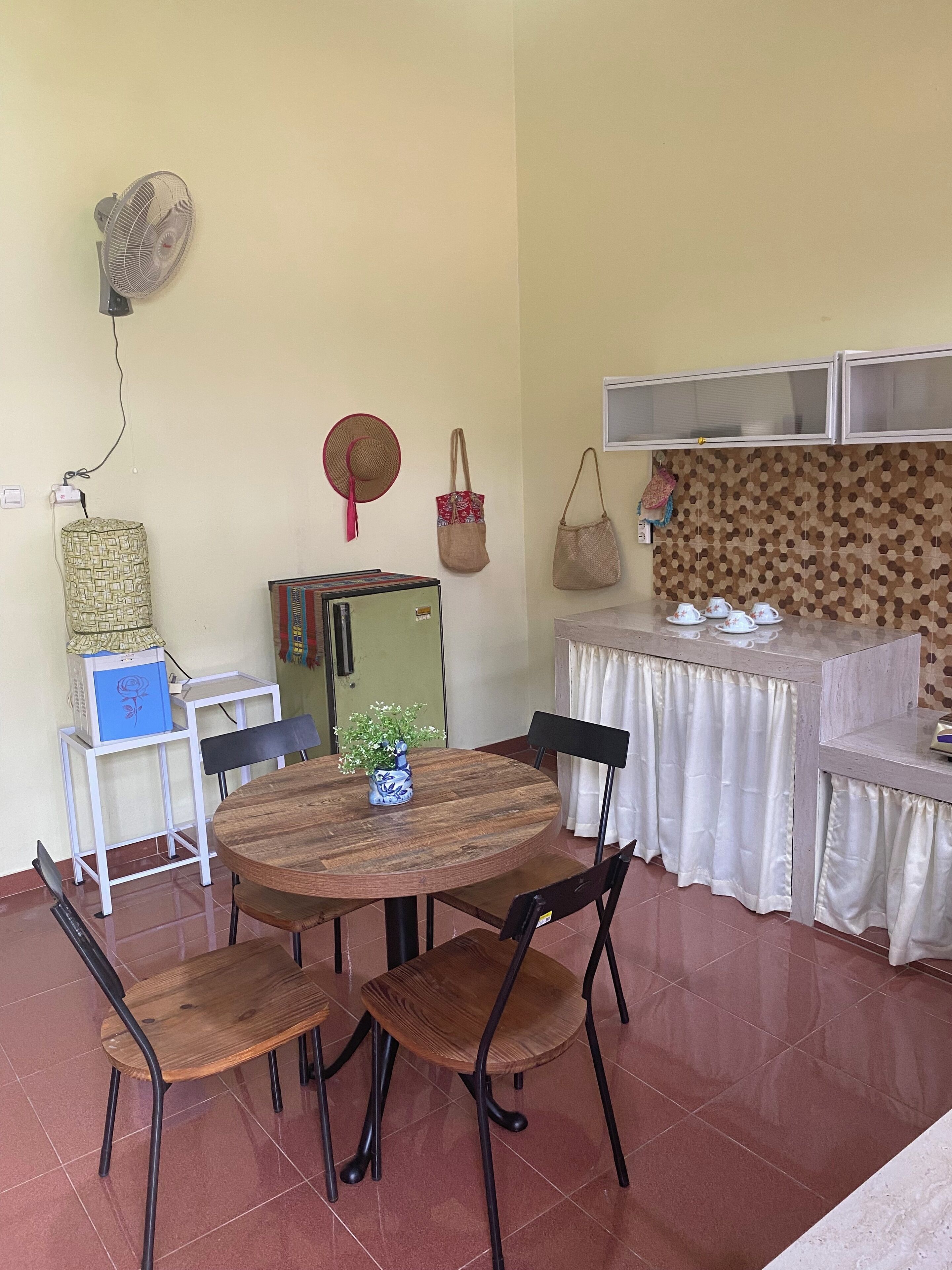 A dining area with a round wooden table, four chairs, a small potted plant, and a white tablecloth.