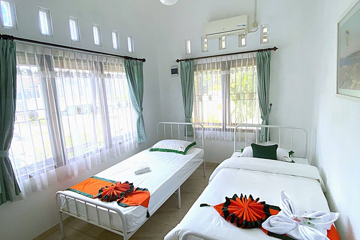 A hotel room with two single beds, a ceiling fan, and a window with curtains.