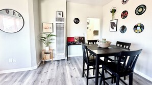 Ruokailutila, jossa on puinen pöytä ja tuolit, kattotuuletin sekä koristeellinen seinätaideteos.