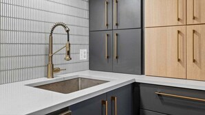 Una cocina con encimera blanca, grifo dorado y armarios con tiradores dorados.