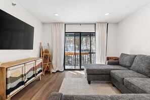 A modern living room with a grey sectional sofa, a wooden console table, and a large flat-screen TV. - White Cap A-406 Ski in Ski Out Condo (Newry)
