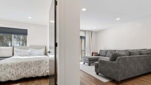 Una habitación moderna con una cama, un sofá gris y un ventanal grande.