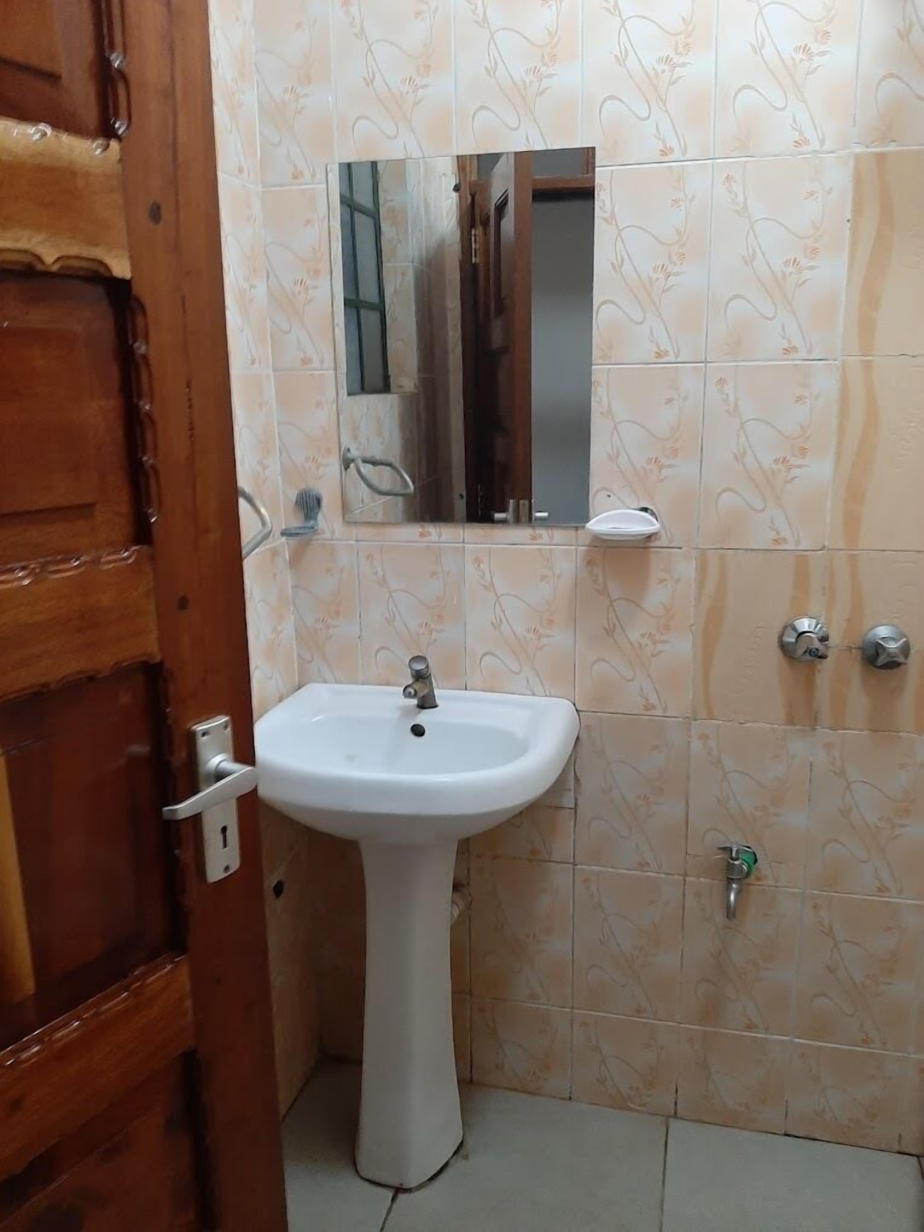 A bathroom with a wooden door, a white sink, a mirror, and patterned tiles.